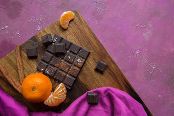 Top view of vegan dark chocolate with mandarin fruits on a wooden cutting board and pink painted...