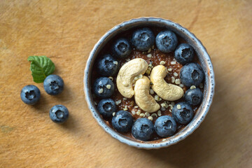 Top view of raw vegan chocolate cake with blueberries and cashews on wooden cutting board  