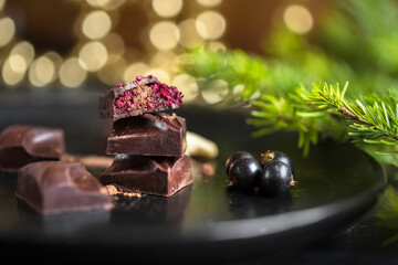 Close up of chocolate vegan candy bars with colourful fillings on wooden cutting board with black currants and Christmas holiday decorations 