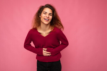 Photo of young delightful happy positive charming brunet wavy woman with sincere emotions wearing casual pink pullover isolated over pink background with empty space and laughing