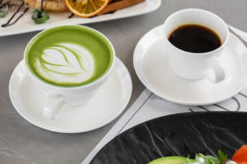 Cup of matcha latte and coffee. High quality photo. Matcha, green tea latte in a cup and croissant. Gray background. Close up. Top view.