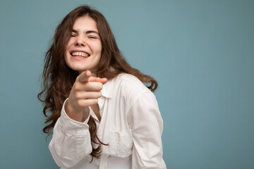 Photo of young positive happy smiling beautiful woman with sincere emotions wearing stylish clothes isolated over background with copy space and pointing at camera