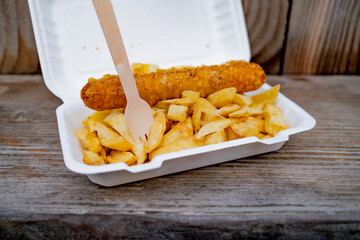 Close and selective focus on a polystyrene carton comprising a battered jumbo sausage and...