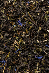 Heap of dry tea leaves. Dried black tea. Textured background of dried leaves of aromatic black tea with blue flowers.