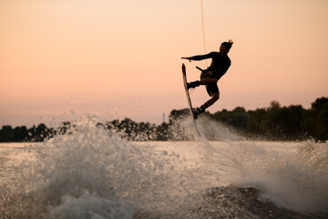active guy jumping over splashing wave on wakeboard holding on to the rope. Water sports activity.