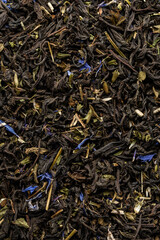 Heap of dry tea leaves. Dried black tea. Textured background of dried leaves of aromatic black tea with blue flowers.