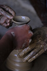 A potter prepares clay Pots or diya on potter's wheel in his residence ahead of Diwali festival. Wet and muddy hands of a craftsman shaping a clay vase on a pottery wheel.