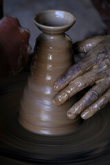  A potter prepares clay Pots or diya on potter's wheel in his residence ahead of Diwali festival. Wet and muddy hands of a craftsman shaping a clay vase on a pottery wheel.
