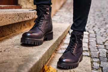 Trendy black leather boots. Close-up stylish shoes. Female legs standing on staircase on street