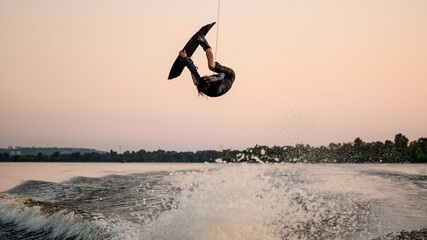 male wakeboarder masterfully jumping and flips on wakeboard over splashing wave