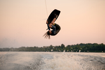 male wakeboarder makes dangerous stunts jumping and flips on wakeboard over splashing wave