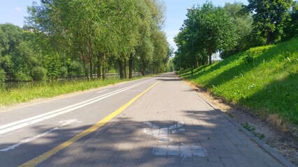 Trees grow along the riverbed that flows through the city, and paved bicycle and tiled pedestrian paths are laid, on which markings are applied. There are lighting poles along them.
