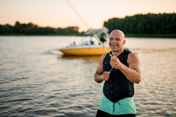 selective focus on smiling man in vest pulling rope against water background