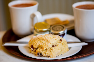 Mugs of tea, jam, butter and a scone with close and selective focus on the scone