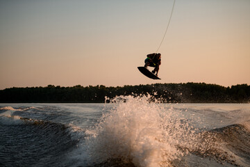 great view of muscular man jumping high with wakeboard over splashing water against the backdrop of sky