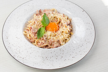 Pasta Carbonara. Spaghetti with bacon, parmesan, cream sauce and egg yolk. Macro close-up isolated on a white round plate. Mediterranean gourmet food.