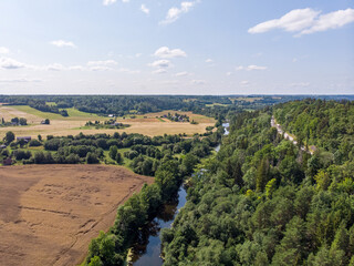 Areal landscape view of small countryside river flowing through agriculture field and forest.