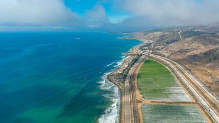 a breathtaking aerial shot of the vast blue ocean water, lush green farmland, cars on the road,...