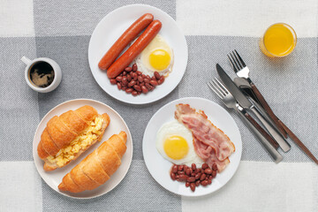 Hearty homemade family breakfast. Eggs, bacon, sausages, beans, croissants, toast and coffee on the table. Top View