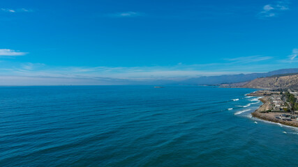 Plakat a breathtaking aerial shot of the vast blue ocean water, cars on the road, majestic mountain ranges, thick cloud cover with blue sky at Rincon Beach in Ventura County California