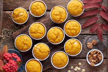 Pumpkin muffins with white chocolate and walnuts. Top view, wooden background. Red rowan