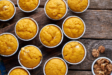 Pumpkin muffins with white chocolate and walnuts. Top view, wooden background.