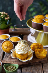 Pumpkin muffins and cupcake with white chocolate and walnuts. Side view, wooden and green background. Hand pours pumpkin seeds onto a cupcake.