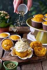 Fototapeta na wymiar Pumpkin muffins and cupcake with white chocolate and walnuts. Side view, wooden and green background. Hand pours pumpkin seeds onto a cupcake.