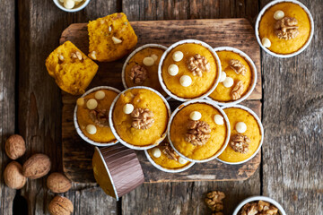Pumpkin muffins with white chocolate and walnuts. Top view, wooden background.