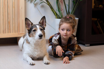 Little cute girl in a plaid dress and a dog play in the room on the floor, child and pet friendship, children and animals.adorable
