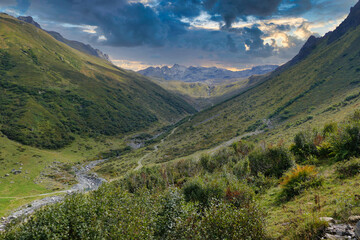 Green valley with a footpath and a mountain stream, high above Gargellen, Vorarlberg, Austria, in the high Alps, under a dark evening sky
