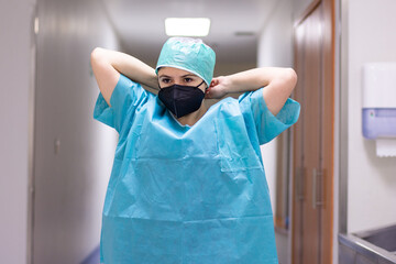 Nurse in a blue gown with a black mask tying her hat