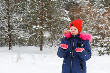 Fototapeta na wymiar Portrait of preteen happy girl in red warm hat catching snowflakes outside on nature winter snowy forest background. Pretty child outdoor, cold weather. Caucasian kid. Teenage riot. Winter joy