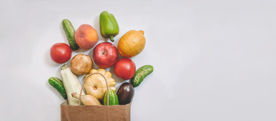 A paper shopping bag with vegetables and fruits, tomato, cucumber, squash, pepper, lemon, eggplant, zucchini, banana, apple, peach on white background