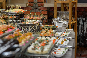 A set of canapes and snack at a banquet with white table. Slices of tomato, olive, cheese, bread and fish on food stand