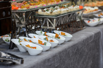A set of canapes and snack at a banquet with white table. Slices of tomato, olive, cheese, bread and fish on food stand