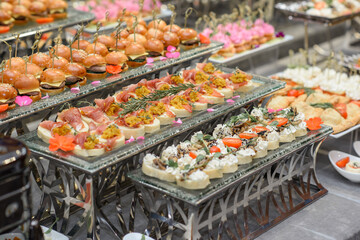 A set of canapes and snack at a banquet with white table. Slices of tomato, olive, cheese, bread and fish on food stand