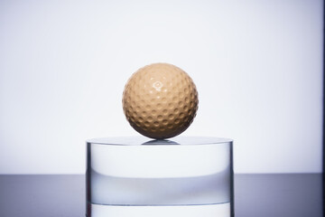 golden golf ball on the transparent glass on color background