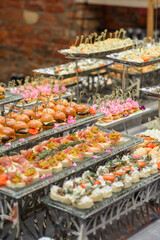 A set of canapes and snack at a banquet with white table. Slices of tomato, olive, cheese, bread and fish on food stand