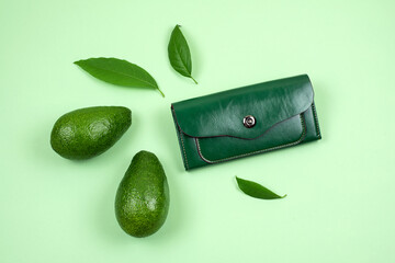 Wallet and avocado on green background. Concept of faux leather made from avocado peel skin,...