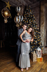 young couple newlyweds laugh rejoice having fun Christmas mood hug tenderness love kiss Christmas tree