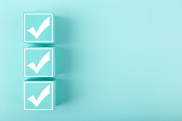 Three white checkmarks on blue cubes against bright pastel blue background with copy space
