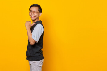 Handsome Asian man cheerful and pointing to empty space isolated on yellow background