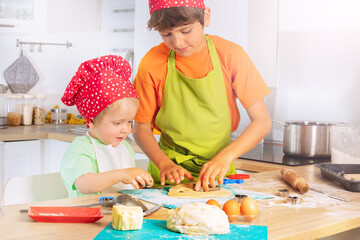 Kids cut out forms from dough for cookies at home