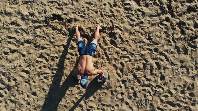 Young fit man doing push ups leaning on two heavy stones placed on sand beach