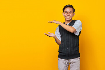 Cheerful asian man showing product over yellow background