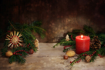 Red candle with fir branches, straw star and nuts as christmas and advent decoration on rustic...