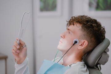 the patient sits in an orthodontist's chair during the tens procedure, looks in the mirror at the electrodes placed on the face
