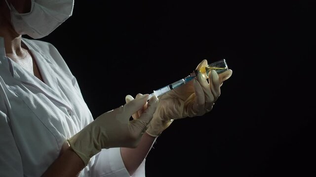 Doctor filling syringe with solution on black background. Nurse wearing protective gloves and mask showing sample of medicine, vaccination against covid-19, laboratory research. Coronavirus vaccine.