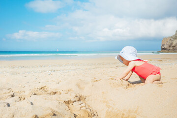 Fototapeta na wymiar Cute baby girl in red swimsuit crawl on sand beach